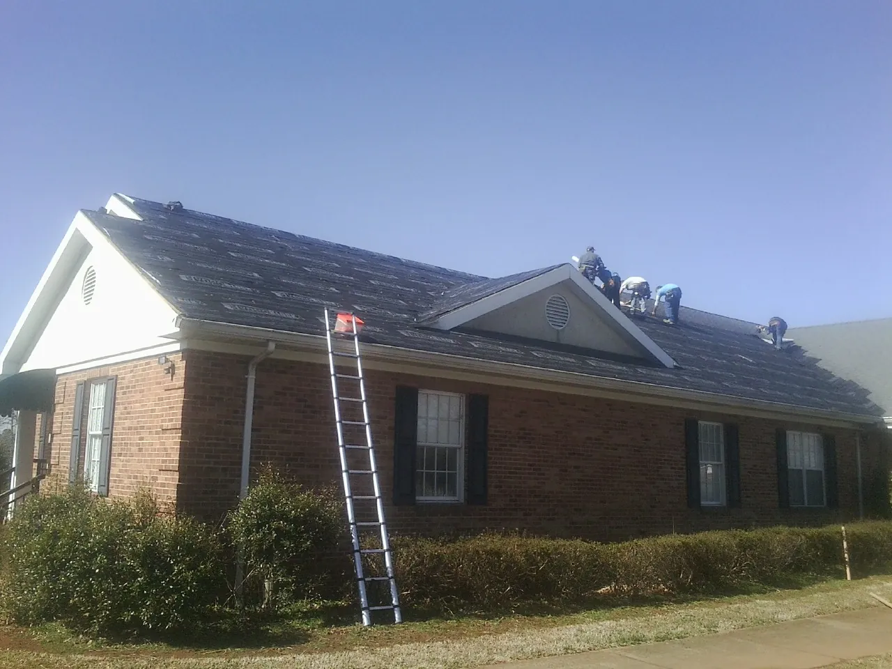 Crew tearing shingles off a brick ranch roof with a ladder set — Metal Roof Repair work by our crew in Farragut