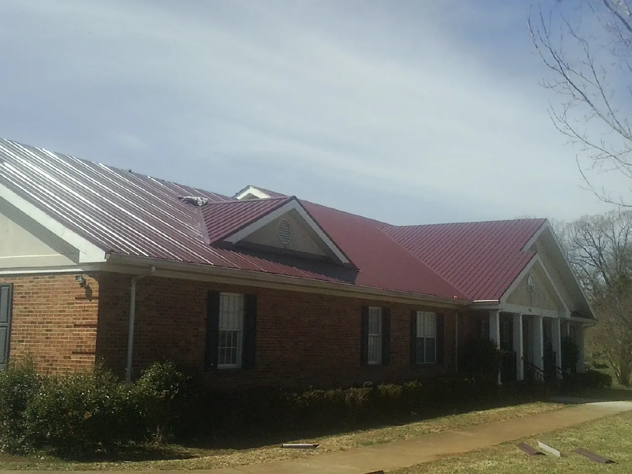 Red metal roof with gabled entries on a long brick building, from a Hail Damage Roof Repair job in Farragut