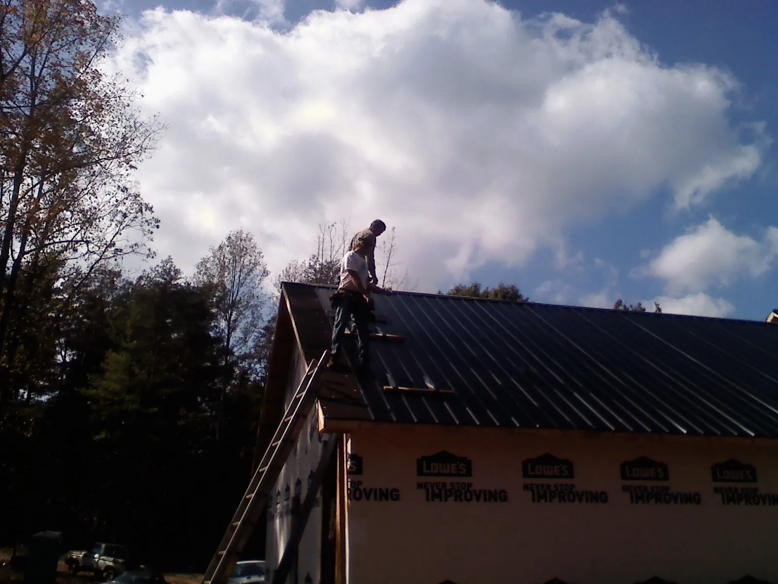 Roofer fastening dark metal panels high against a cloudy sky, from a Roof Inspection job in Farragut