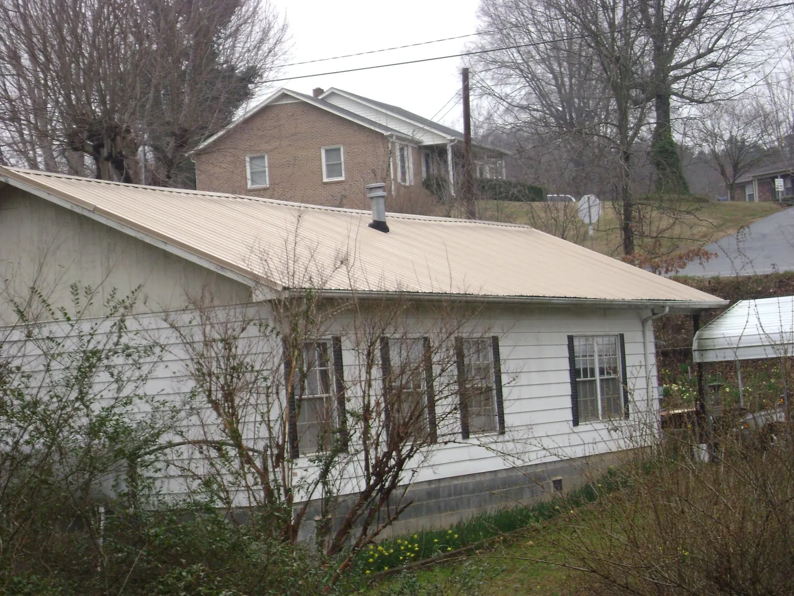 Tan metal roof on a white sided house set into a hillside — Commercial Roofing by Roofing Brothers in Farragut